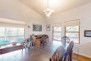 A dining area with a wooden table and chairs, a chandelier, and large windows with blinds. - Under The Stars - Shaver Lake (Shaver Lake)