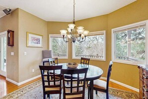 A dining room with a chandelier, wooden chairs, a round table, and large windows with a view of trees. - Mule Deer Cabin - Pine Mountain Lake (Groveland)
