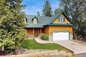 A two-story house with a green roof, a front porch, and a garage. - Mule Deer Cabin - Pine Mountain Lake (Groveland)