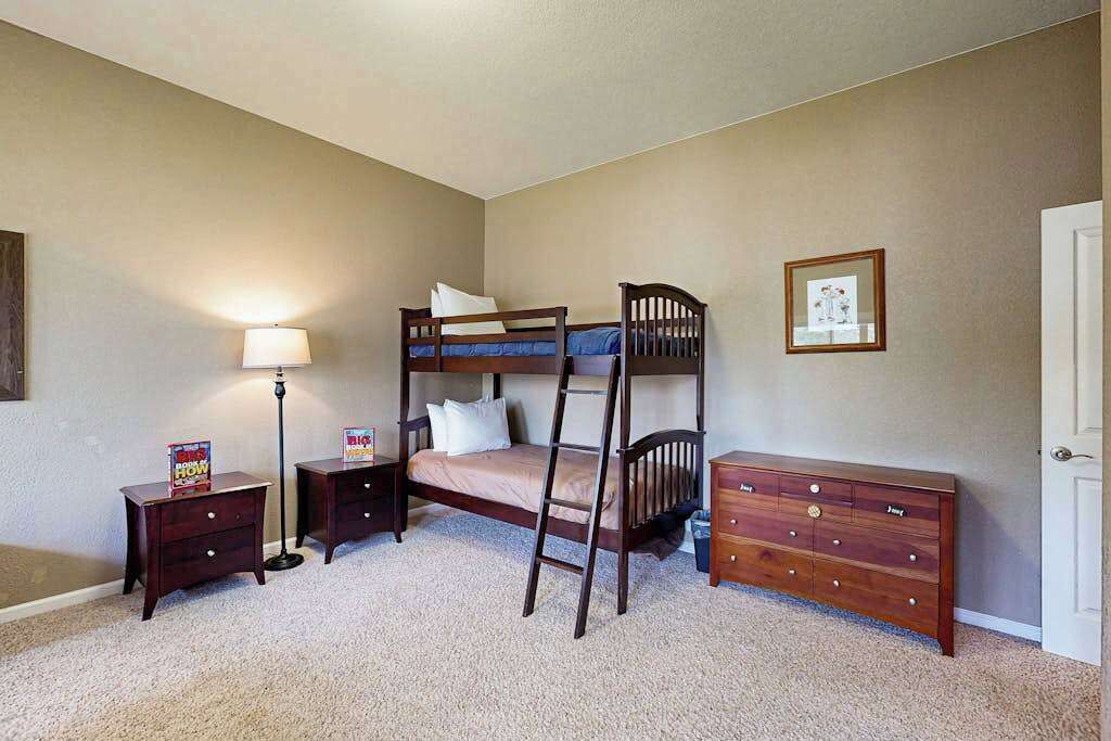 A bedroom with a bunk bed, bedside tables, a dresser, a lamp, and a framed picture on the wall.