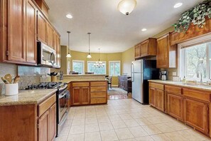 A kitchen with wooden cabinets, a granite countertop, a stove, a refrigerator, and pendant lighting. - Mule Deer Cabin - Pine Mountain Lake (Groveland)