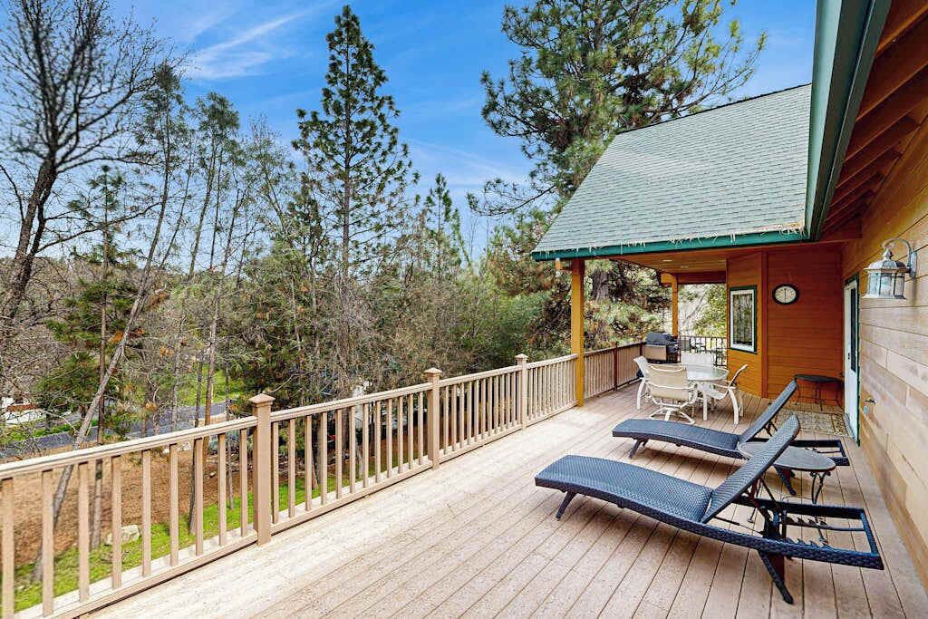 A wooden deck with lounge chairs and a table, surrounded by a wooden fence and trees.