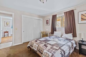 Ein Schlafzimmer mit Bett, Schreibtisch, Stuhl, einem Fenster mit Vorhängen und einer Tür.