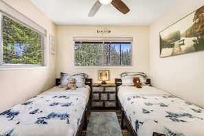 A bedroom with two beds, a ceiling fan, a window with a view of trees, and a framed picture on the wall. - Paws Place - Blue Lake Springs (Arnold)