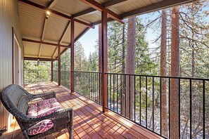 A covered deck with a wicker chair and a view of tall trees. - Paws Place - Blue Lake Springs (Arnold)