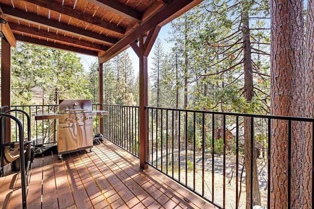 Um terraço coberto ao ar livre com churrasqueira, cercado por grade de metal, com vista para uma área arborizada.
