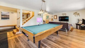 Ein Billardtisch in einem Raum mit Holzdielen, einer Treppe, einem Fernseher und Wanddekorationen.