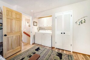 A laundry room with a washing machine, dryers, and a wooden door. - Paws Place - Blue Lake Springs (Arnold)