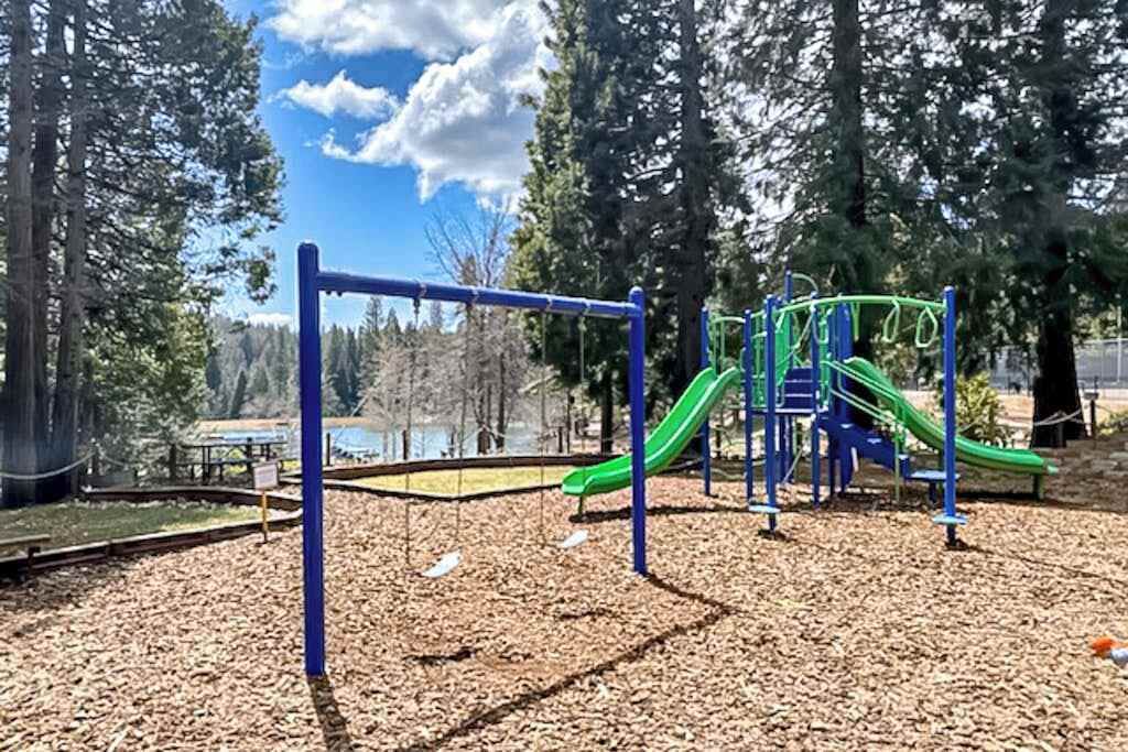 A playground with a slide and climbing structures, surrounded by trees and a clear sky.