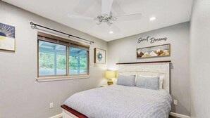 Un dormitorio con una cama, un ventilador de techo, una ventana y obras de arte en las paredes.