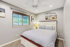 Ein Schlafzimmer mit einem Bett, einem Deckenventilator, einem Fenster und Kunstwerken an den Wänden.