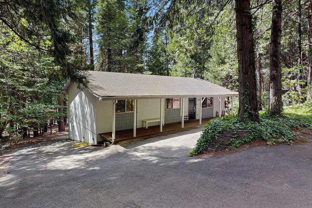 A small, single-story building with a porch, surrounded by tall trees.