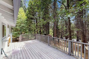 A wooden deck with a railing, surrounded by a forested area. - Meadowview Cabin - family friendly, W&D (Arnold)