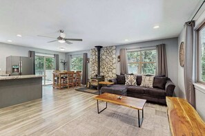 A modern living room with a stone fireplace, a sofa, a coffee table, and a dining area with a table and chairs. - Meadowview Cabin - family friendly, W&D (Arnold)