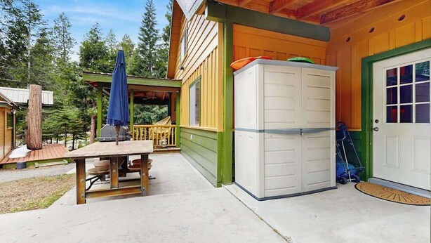 A wooden cabin with a covered patio, a refrigerator, and a door with a window. - Dorabella Cabin - East Village (Shaver Lake)