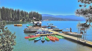 A lakeside dock with colorful canoes and a small building with a flag. - Dorabella Cabin - East Village (Shaver Lake)