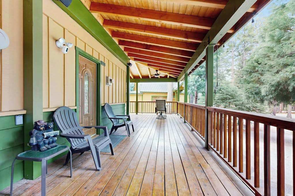 Une terrasse en bois avec deux chaises et une table, une porte verte et une rambarde donnant sur une zone boisée.