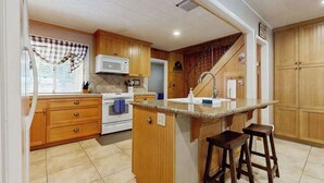 A kitchen with wooden cabinets, a central island with stools, a microwave, and a stove. - Dorabella Cabin - East Village (Shaver Lake)