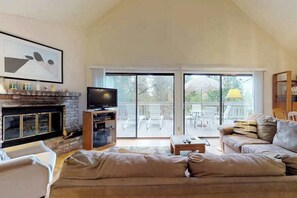 A living room with a fireplace, a television, a sofa, and a sliding glass door leading to an outdoor patio.