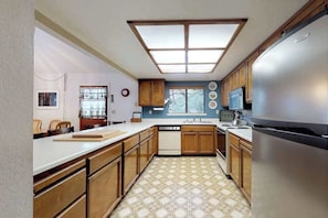 A kitchen with wooden cabinets, a stainless steel refrigerator, a dishwasher, and a window with blinds. - Forest Chalet - Pine Mountain Lake (Groveland)