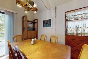 A dining area with a wooden table and chairs, a wooden cabinet, a framed picture on the wall, and a window with curtains.