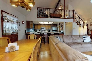 A spacious living area with a wooden dining table, a sofa, and a kitchen in the background. - Forest Chalet - Pine Mountain Lake (Groveland)