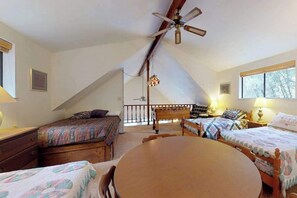 A cozy attic bedroom with two beds, a dining table, and a ceiling fan.