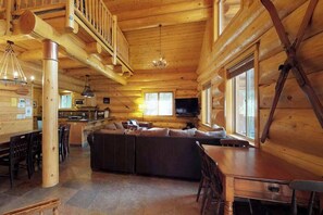 A log cabin interior with a dining area, a living room with a sofa, and a kitchen area. - Logger's Landing - Huntington Lake (Lakeshore)