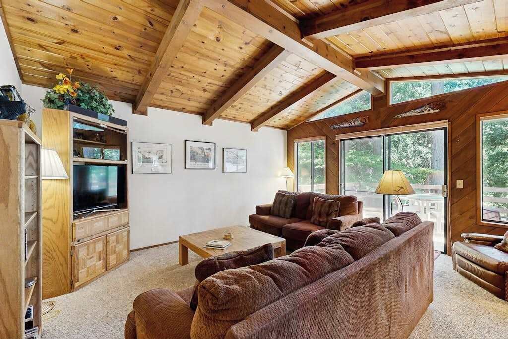 Een gezellige woonkamer met houten plafond, een televisie, een bank en een bijzettafeltje.