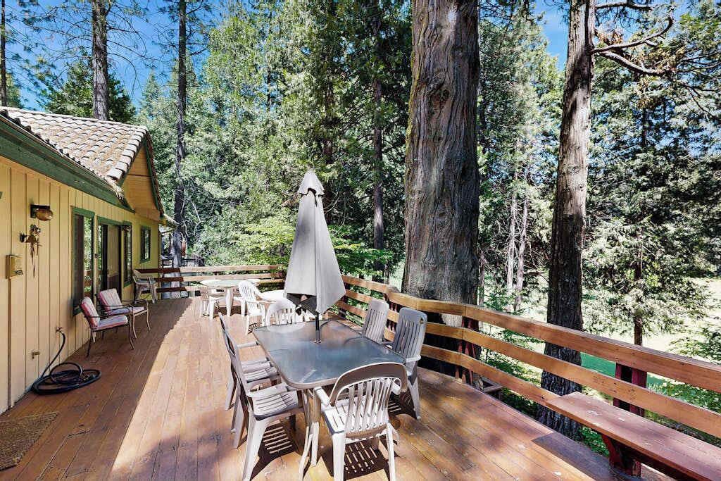 A wooden deck with outdoor seating, surrounded by tall trees.