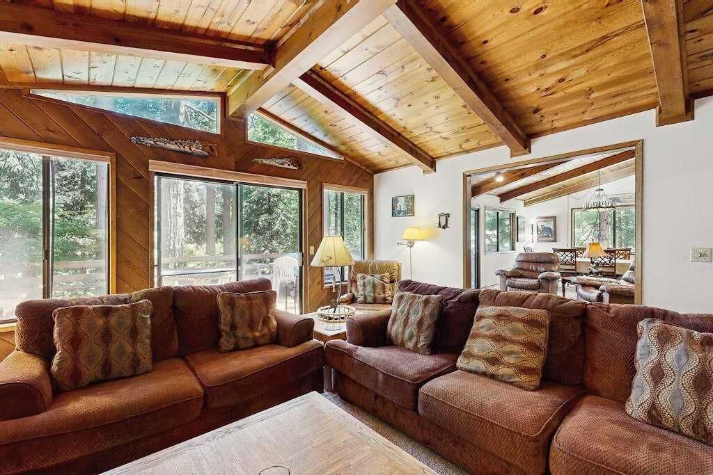 Una sala de estar acogedora con un sofá seccional, ventanas amplias y techo de madera.