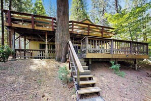 A rustic cabin with a wooden staircase leading to a deck, surrounded by trees.