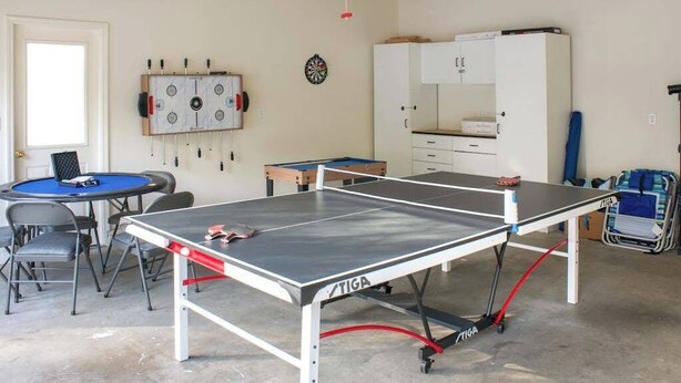 Ein Tischtennistisch mit TIGA-Logo, eine Dartscheibe, ein Fußballtisch und ein Schrank in einem Raum mit Betonboden.