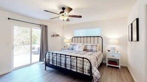 Ein Schlafzimmer mit einem Bett, Deckenventilator, Nachttisch, Fenster mit Jalousien und einer Tür zu einem Außenbereich.