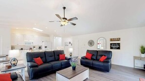 Ein modernes Wohnzimmer mit einer schwarzen Ledersofa-Garnitur, einem Holztisch und einem Deckenventilator.