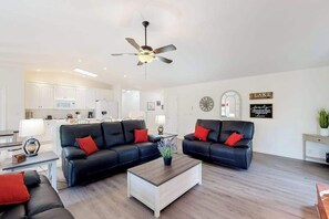 Ein modernes Wohnzimmer mit einer schwarzen Ledersofa-Garnitur, einem Holztisch und einem Deckenventilator.