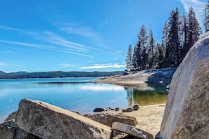 A natural landscape with a calm lake, rocky shoreline, and dense forest. - Tranquil Pines Retreat - Ridgetop (Shaver Lake)
