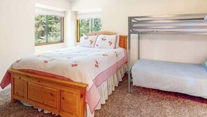 A bedroom with a wooden bed, a bunk bed, and two windows with a view of greenery. - Tranquil Pines Retreat - Ridgetop (Shaver Lake)