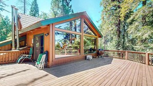 A wooden deck with a covered seating area, a grill, and a view of the surrounding forest. - Tranquil Pines Retreat - Ridgetop (Shaver Lake)