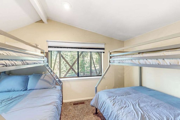 A room with bunk beds, a window with a view of trees, and a ceiling fan. - Tranquil Pines Retreat - Ridgetop (Shaver Lake)