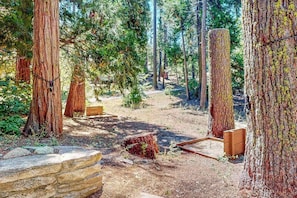 A forested area with large trees, a dirt path, and wooden structures. - Tranquil Pines Retreat - Ridgetop (Shaver Lake)