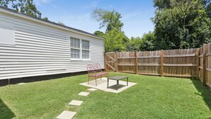 A backyard with a white mobile home, a wooden fence, a red metal bench, and a small table. - Main House + Modern Tiny Home - 4 BR / 3 BA (Nacogdoches)