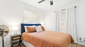 A bedroom with a bed, a bedside table with a lamp, a standing fan, and a ceiling fan. - Main House + Modern Tiny Home - 4 BR / 3 BA (Nacogdoches)