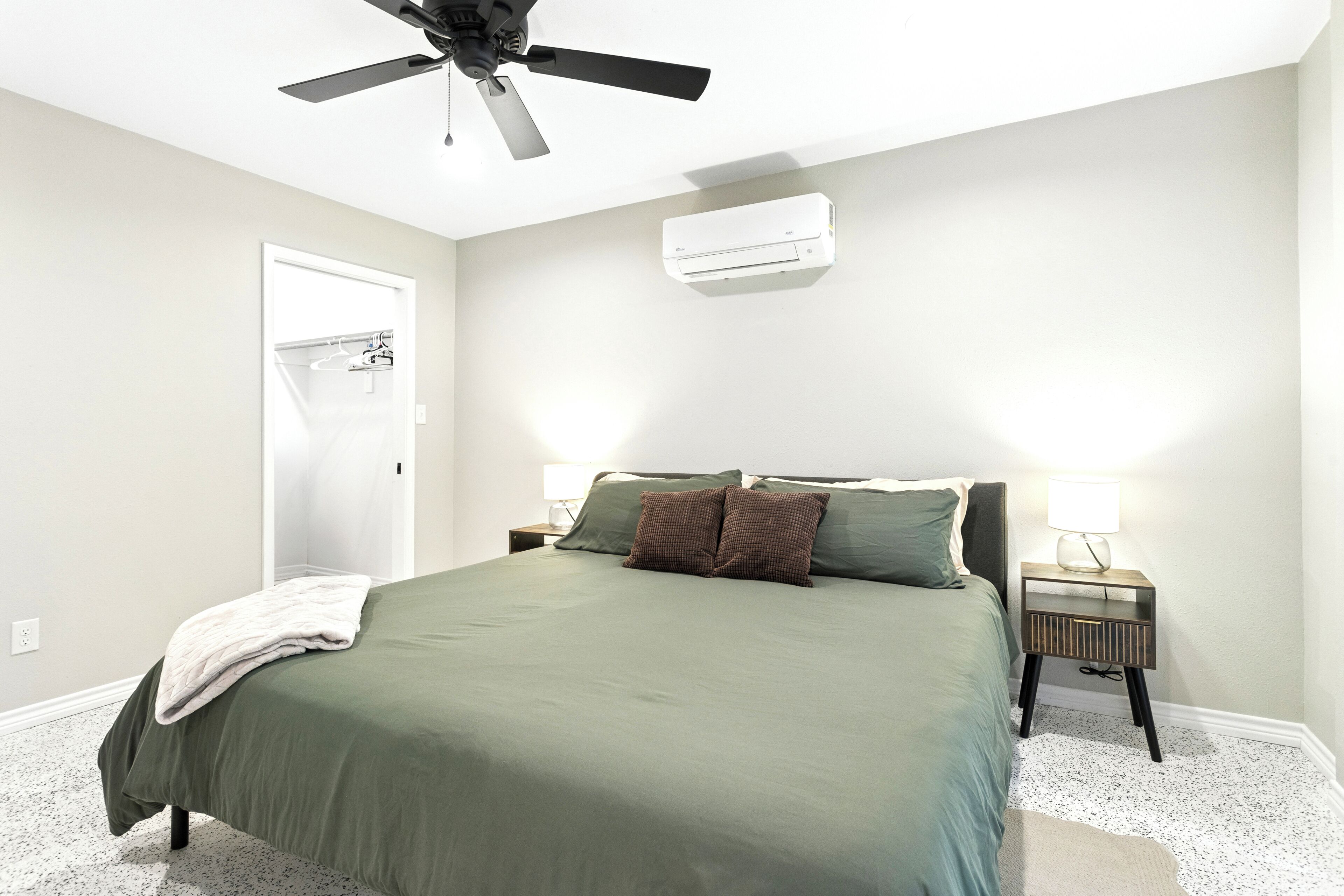 A bedroom with a bed, two bedside tables with lamps, a ceiling fan, and an air conditioning unit.