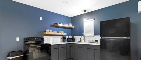 A compact kitchen with dark blue walls, a black refrigerator, a stove, and a microwave.