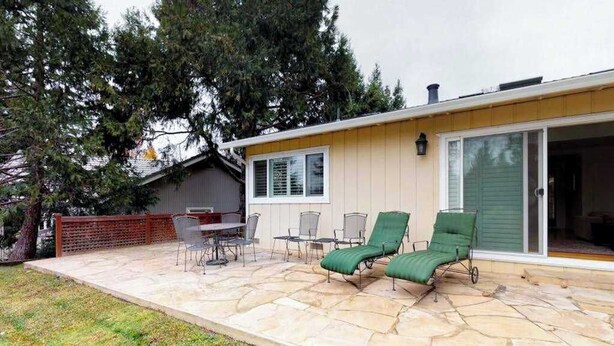 Un patio con piso de piedra, mobiliario exterior y un ventanal corredizo que da a un espacio cubierto.