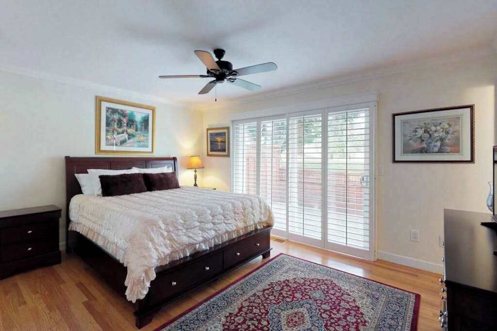 Un dormitorio con cama, ventilador de techo, ventana con persianas y alfombra.