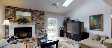 A living room with a fireplace, sofa, television, and a ceiling fan.