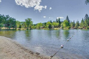 A lake with a sandy shore, surrounded by trees and buildings in the background. - Greenside Getaway - Pine Mountain Lake (Groveland)