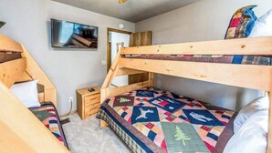 Habitación con literas, un televisor, una mesita de noche pequeña y un ventilador de techo.